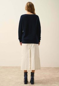 Granatowy sweter robiony na drutach o luźnym kroju, w zestawieniu z białą spódnicą midi z centralnym rozcięciem i niebieskimi botkami na obcasie, widok z tyłu.