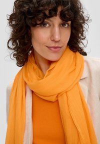 Leichter orangefarbener Schal, der um den Hals drapiert ist, über einem passenden orangefarbenen Oberteil. Weiche, leicht zerknitterte Textur, lässiger Stil.