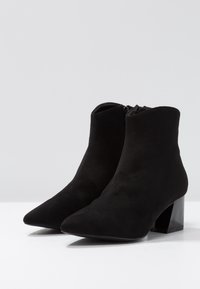 Botines de ante negros con punta afilada, cierre de cremallera y tacón cuadrado, con una textura suave y un diseño minimalista.