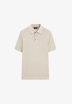 Polo en coton beige avec manches courtes, patte de boutonnage à trois boutons et col côtelé. Texture douce avec un design minimaliste.