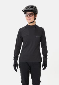 Maglietta tecnica nera a maniche lunghe con colletto alto, aperture per il pollice e texture liscia, abbinata a guanti neri e un casco.