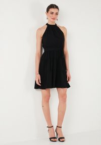 Robe noire à col halter avec un corsage ajusté, une jupe à volants et un détail de ceinture. Tissu lisse avec une texture douce et fluide.