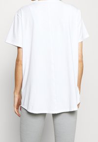 Camiseta blanca de manga corta hecha de tejido suave. Presenta un corte holgado, escote redondeado y un dobladillo recto con una costura central en la parte trasera.
