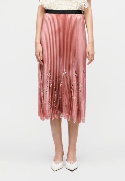 Jupe midi plissée en satin rose doux avec une ceinture noire, ornée d'une broderie florale à l'ourlet et une texture lisse et brillante.