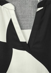 Svart och vit mönstrad tyg med v-ringad design, med slät textur, kontrasterande färger och synlig sömnadsdetalj.