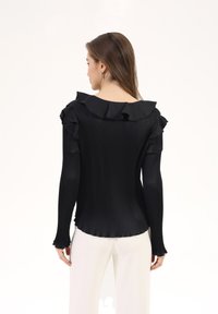 Black ribbed long-sleeve top with a wide ruffled neckline and flared cuffs. The back is fitted and smooth, highlighting its sleek design.