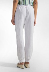 Białe lniane spodnie o luźnym kroju, z elastycznym pasem i ściągaczami przy nogawkach. Posiadają boczną kieszeń typu cargo dla dodatkowej funkcjonalności.