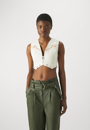 Canottiera bianca corta con zip frontale, caratterizzata da cuciture decorative e hardware in metallo, abbinata a pantaloni plissettati verdi oliva a vita alta.
