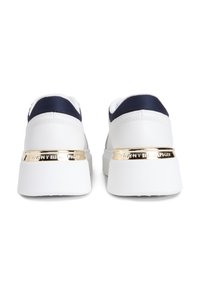 Λευκά αθλητικά παπούτσια με μπλε ναυτικό λεπτομέρειες, διαθέτουν υφασμένη επιφάνεια, ανυψωμένη φτέρνα και μεταλλική χρυσή ετικέτα του εμπορικού σήματος στο πίσω μέρος.