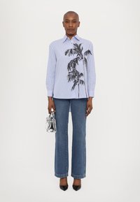 Blau-weiß gestreiftes Hemd mit Palmenmotiv, kombiniert mit hochgeschnittenen Jeans, einer silbernen Handtasche und spitzen schwarzen High Heels.