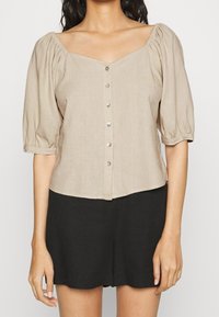 Kortärmad beige blus med fyrkantig halsringning, knappstängning framtill och rynkade ärmar. Slät tyg med en något texturerad yta.