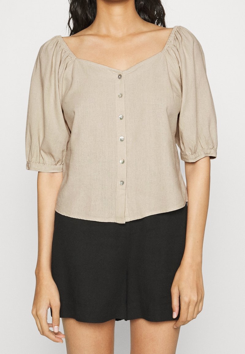 Kortärmad beige blus med fyrkantig halsringning, knappstängning framtill och rynkade ärmar. Slät tyg med en något texturerad yta.