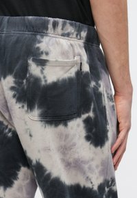 Φόρμες φλις με μοτίβο tie-dye σε μαύρο, γκρι και άσπρο χρώμα. Διαθέτουν ελαστική μέση και πίσω τσέπη. Μαλακή υφή.