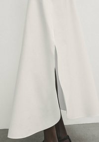 Gonna bianca fluida con taglio asimmetrico e spacco laterale. Il tessuto appare liscio, leggero e presenta un design pulito e minimalista.