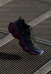 Black sneaker with textured upper, purple midsole, and circular BOA lacing system. Features a rounded design and contrasting accent colors.