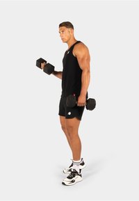 Spierige man in zwarte sportkleding die zwarte halters optilt, staande tegen een effen witte achtergrond, gefocust op zijn training.