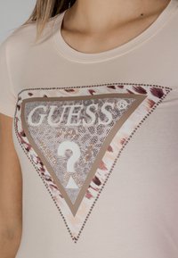 Roosa sobiv t-särk, millel on suur kolmnurkne logo tekstuurse disainiga, metallsed aktsendid ja leopardiprindiga äär.
