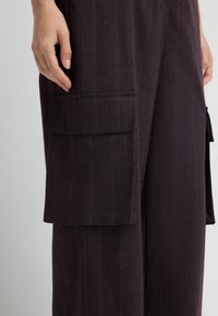 Pantalones de rayas finas en color púrpura oscuro con una tela texturizada, que cuentan con un bolsillo plano en el costado y ligeros detalles de sastrería.