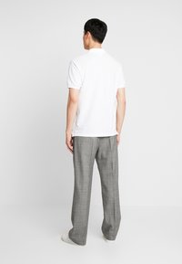 Polo blanc à manches courtes, porté avec un pantalon large à motifs à carreaux gris. Texture lisse, design minimaliste, associé à des baskets blanches.