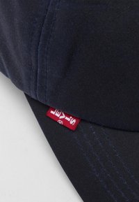 Boné de algodão azul-marinho com um design estruturado, apresentando uma etiqueta vermelha da Levi's ao lado e detalhes de costura visíveis.