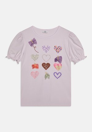 Camiseta de color púrpura claro con mangas abullonadas que presenta varios apliques decorativos en forma de corazones y lazos en múltiples colores y texturas.