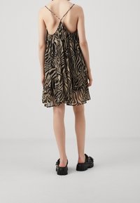 Vestido sin mangas de estampado negro y beige con un dobladillo con volantes y espalda descubierta, combinado con zapatos de plataforma negros y gruesos.