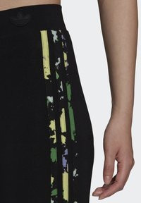 Mustat urheiluhousut, joissa on teksturoitu vyötärö, sivuilla keltaiset, vihreät ja violetit raidat, logo ylhäällä ja istuva leikkaus.