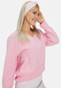 Pullover rosa chiaro a scollo a V realizzato in materiale morbido, con maniche lunghe e svasate e orlo a coste. Indossato con un cerchietto abbinato rosa chiaro.