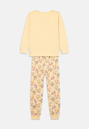 Chemise à manches longues jaune avec un col rond et un pantalon de pyjama jaune assorti présentant un motif de divers personnages de dessin animé sur un fond clair.