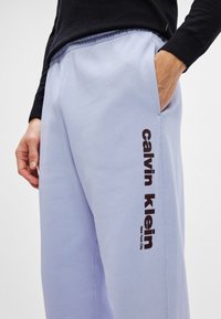 Απαλές απλές μπλε φόρμες με πλευρική τσέπη, που διαθέτουν εκτύπωση μαύρου λογότυπου στο αριστερό πόδι. Φτιαγμένες από μαλακό ύφασμα με ελαστική μέση.