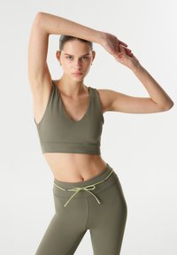 Olijfgroen sportieve crop top met V-hals, gemaakt van een gladde stof. Gecombineerd met bijpassende strakke leggings met een trekkoord in de taille.