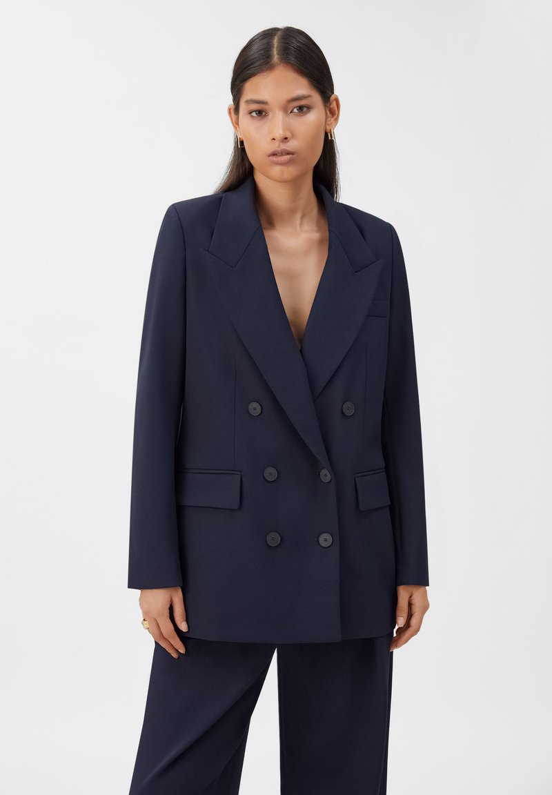 Marineblauer, doppelt geknöpfter Blazer aus glattem Stoff, mit großen Revers, zwei Fronttaschen und sechs passenden Knöpfen.