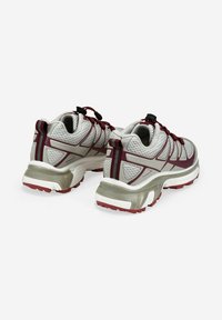 Par de zapatillas deportivas grises y burdeos con tela de malla, suelas gruesas y lengüetas, mostradas desde la parte de atrás sobre un fondo blanco.