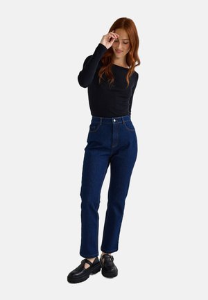 Jean taille haute bleu foncé, coupe droite, associés à un haut noir à manches longues côtelé et des chaussures à plateforme noires.
