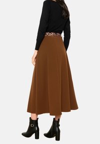 Bruine A-lijn rok met een luipaardprint tailleband, gedragen met een zwart top met lange mouwen en zwarte enkellaarsjes. Gladde stof, lengte tot halverwege de kuit.