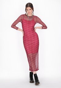Långärmad kläddress i genomskinlig magenta mesh med svarta leopardfläckar, med en sidan slit och lagerdesign. Bärs med svarta snörstövlar.