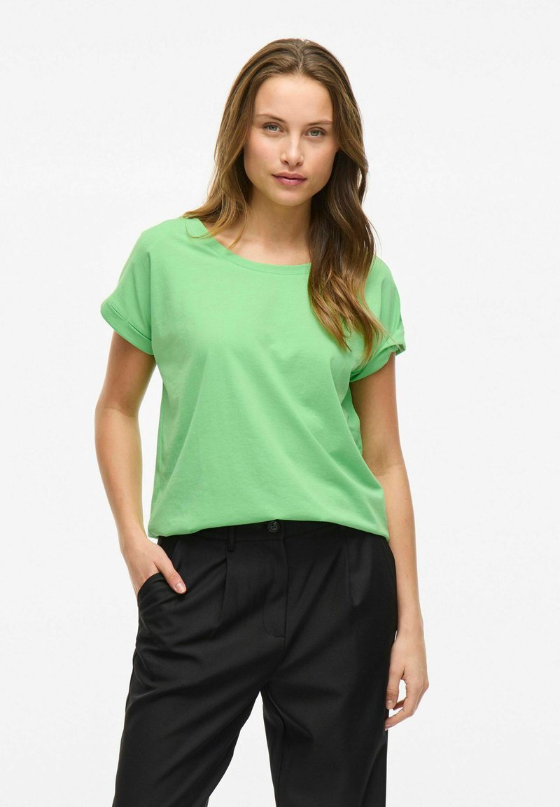 Grön bomullströja med uppvikta korta ärmar och rundad halsringning, kombinerad med svarta skräddarsydda byxor med veck och sidofickor.