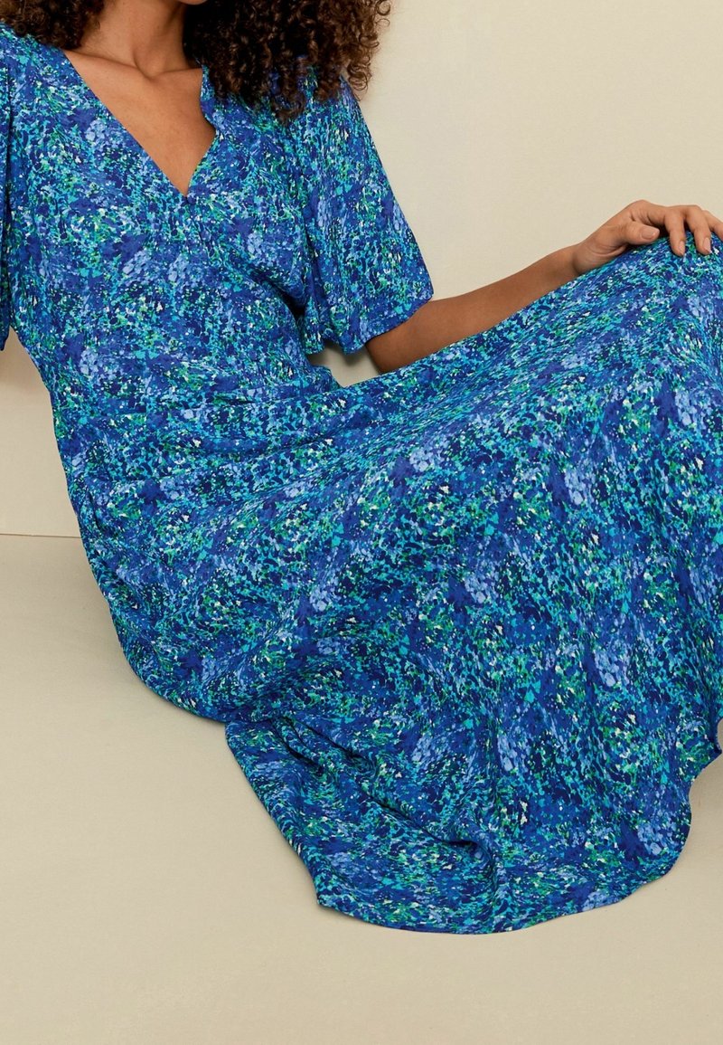 Robe maxi bleue à fleurs avec un décolleté en V, des manches courtes et un motif tourbillonnant de nuances de vert, de bleu et d'accents blancs. Texture de tissu douce et fluide.