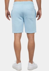 Shorts bleu clair en tissu doux, dotés d'une taille élastique, d'une poche arrière et de finitions à ourlet. Associés à des baskets blanches.