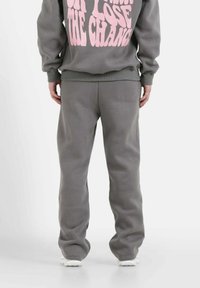 Sudadera gris y pantalones de chándal a juego que presentan un corte relajado, con un texto rosa destacado en la parte posterior, fabricados en una tela suave sin patrones visibles.