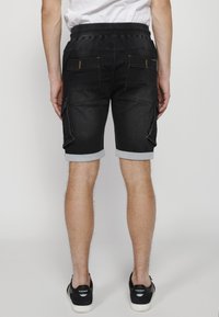 Pantalones cortos de mezclilla negra con un acabado ligeramente desgastado, con costuras en contraste, puños enrollados y varios bolsillos en los lados.