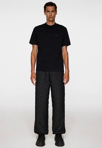 Svart T-shirt med korta ärmar och en minimalistisk logotyp, kombinerad med texturerade svarta quiltade byxor, bärs med svarta klumpiga skor.