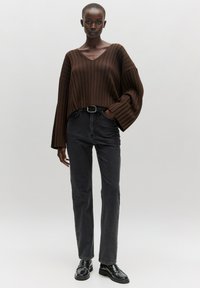 Brown ribbed knit oversized sweater with a V-neck, wide sleeves; paired with high-waisted black straight-leg jeans and black loafers.