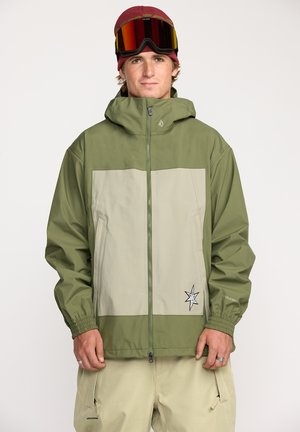 Veste coupe-vent verte et beige avec capuche, dotée de poignets élastiques, d'un zip sur le devant et d'un badge logo à l'ourlet. Texture lisse.