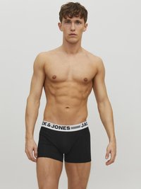 Schwarze Boxer-Shorts mit einem weißen elastischen Bund, auf dem der Text "JACK & JONES" steht. Der Stoff ist glatt und enganliegend, was die Figur des Modells betont.