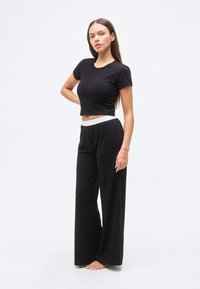 Μαύρο κοντό t-shirt και φαρδιά μαύρη παντελόνα με λευκή μέση. Λείος υφασμάτινος υφή, casual σχεδιασμός. Χωρίς μοτίβα ή επιπλέον λεπτομέρειες.