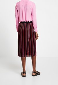 Gonna midi a righe nere e rosse con una cintura elastica nera, abbinata a una maglietta rosa a maniche lunghe e sandali neri con borchie.