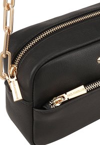 Zwarte leren schoudertas met een gouden ketting en ritsaccenten. Heeft een gestructureerd oppervlak en een gemerkte ritstrekkers.