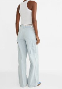 Pantalones cargo de rayas azul claro y blanco, con piernas anchas, que cuentan con bolsillos laterales, una cintura alta y un cierre de botón en la parte trasera.