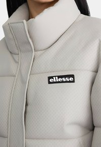 Giacca piumino grigia chiara con colletto alto, design trapuntato e texture a pois. Presenta un logo ellesse nero sul davanti.
